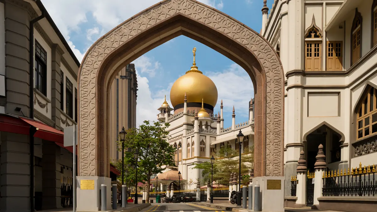 The golden dome of Sultan Mosque framed through an ornate Moorish archway in Kampong Glam