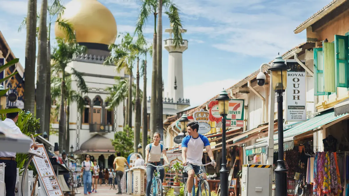 Cyclists riding past shops and restaurants on Bussorah Street below Sultan Mosque