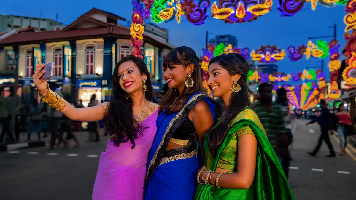 Little India — Three women in brightly coloured saris taking a photo beneath Deepavali decorations in Little India