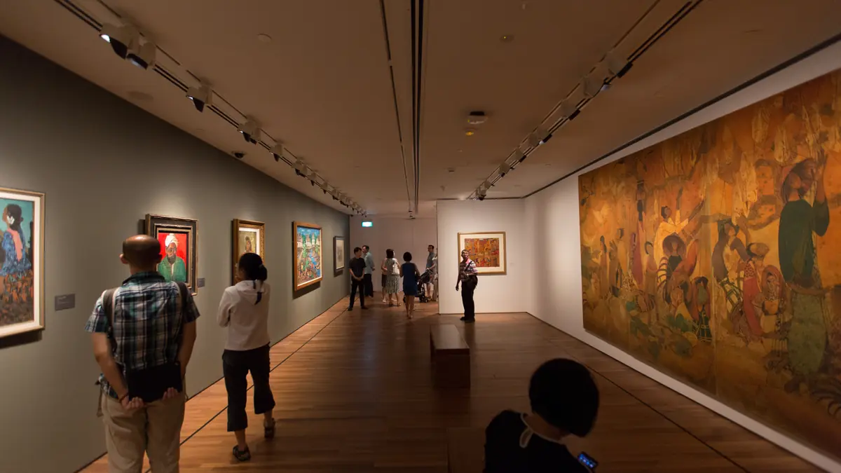 National Gallery Singapore — Visitors walking a spotlit gallery of framed paintings on wooden floors at National Gallery Singapore