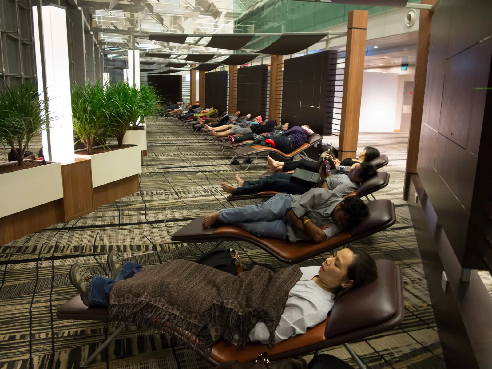 Travellers resting on loungers in a free-to-use Snooze Lounge in the transit area at Changi Airport
